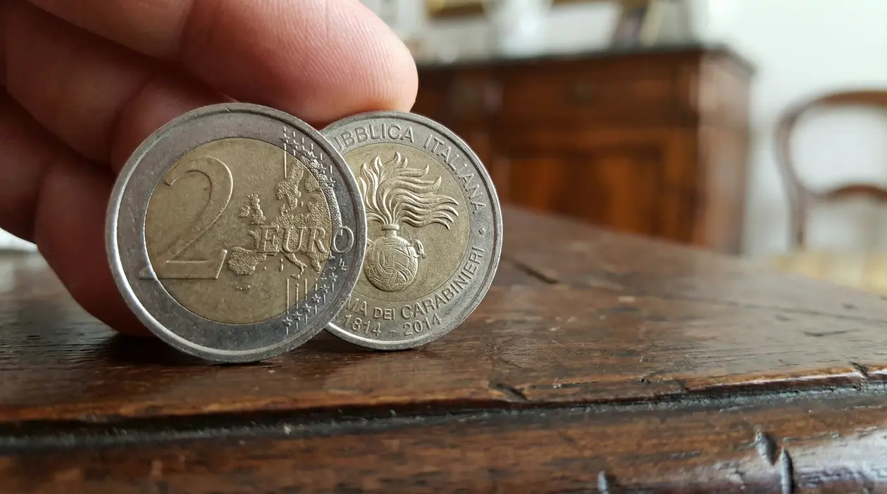 Moneta da 2 euro commemorativa con simbolo delle forze dell'ordine tenuta da una mano