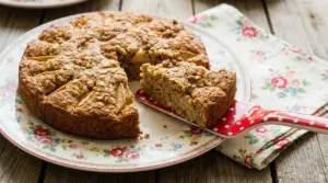 Torta di mele con avena e noci su un piatto floreale, con una fetta tagliata su una paletta rossa